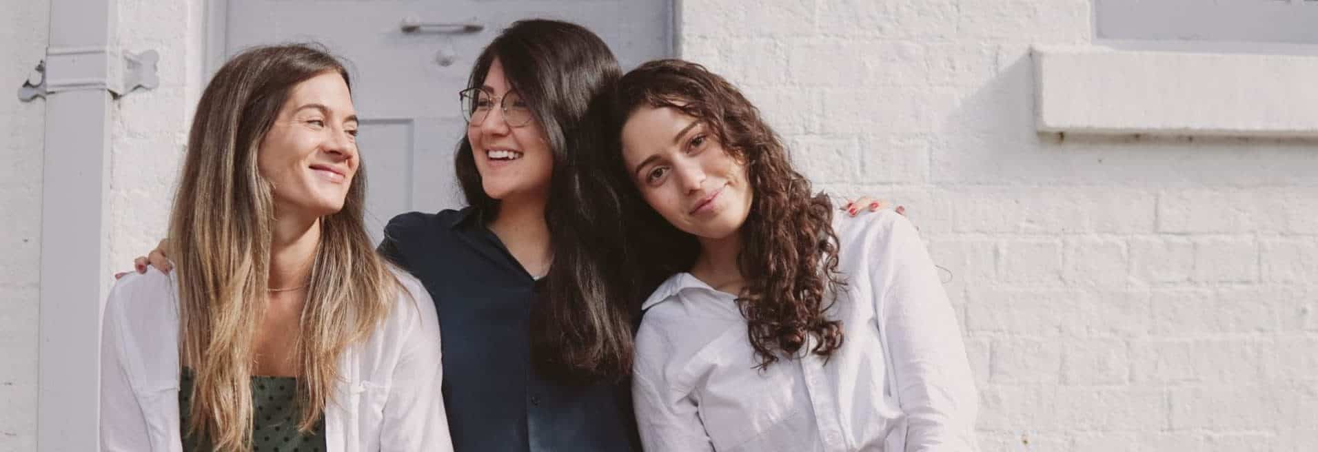 Three young women smiling together in front of a home